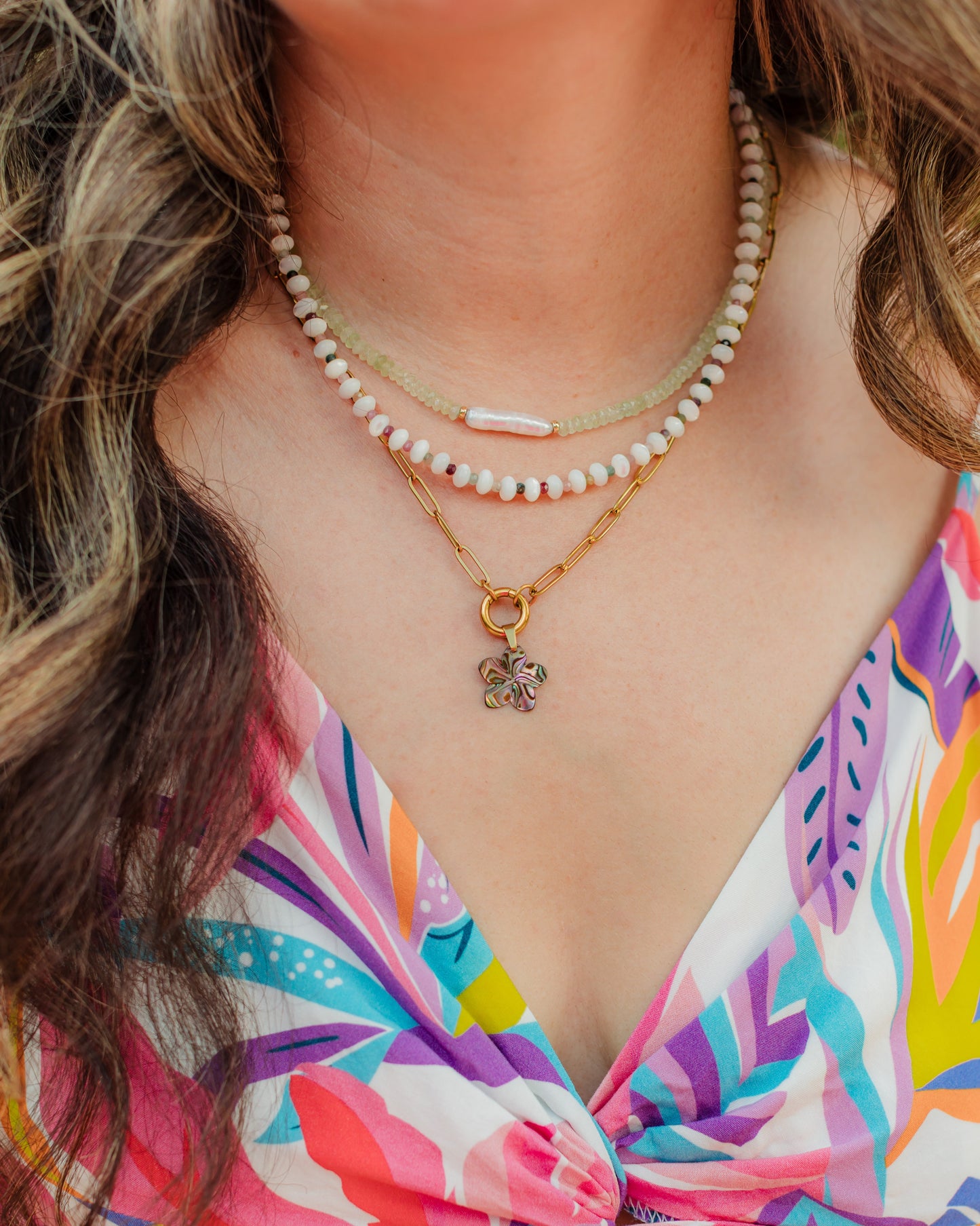 Woman wearing the Maui Bloom abalone shell flower necklace in a colorful layered coastal jewelry look