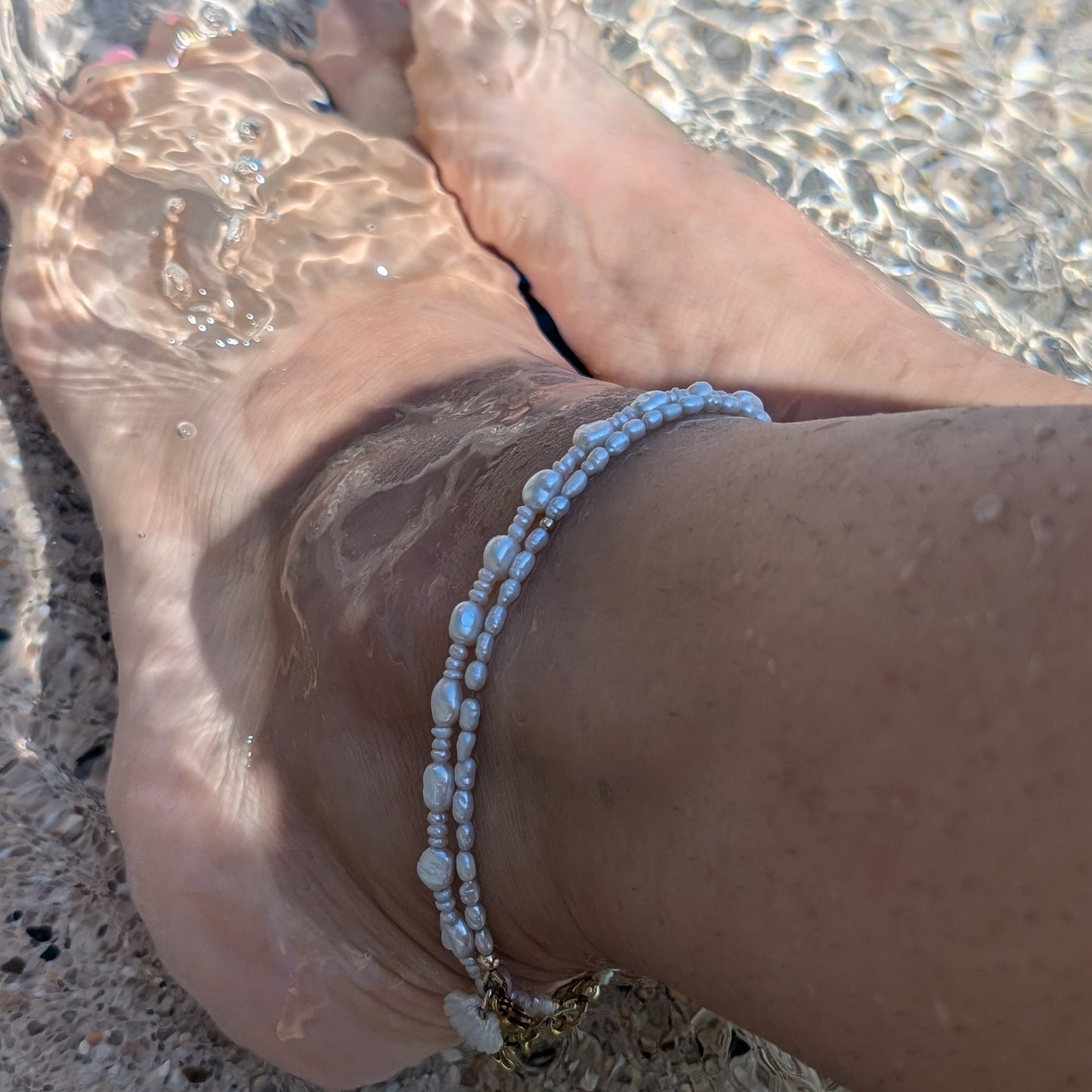 Layered pearl anklet styled with gold jewelry for a coastal summer look