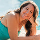 Woman in a turquoise dress lying by a pool wearing pink pearl jewelry