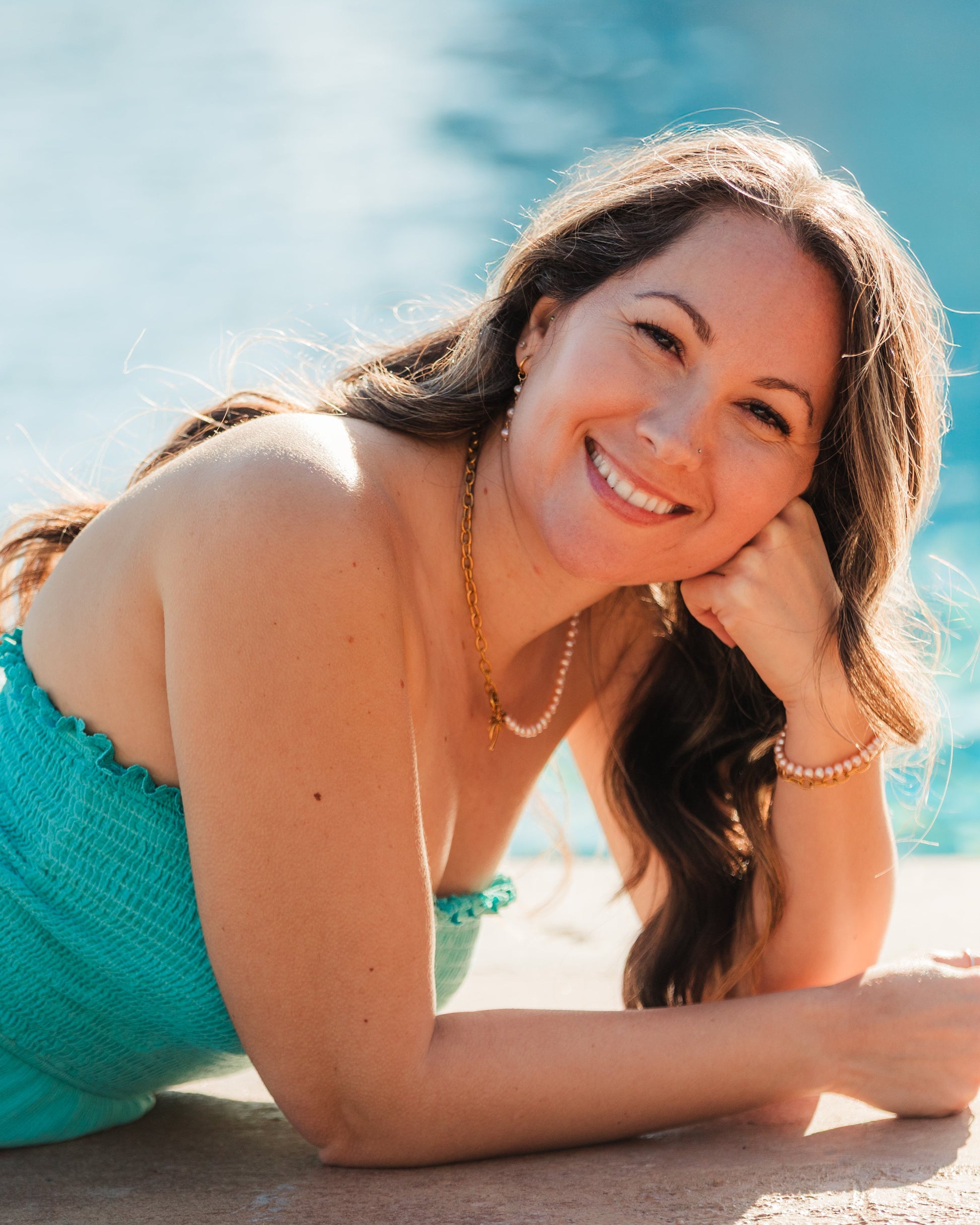 Woman in a turquoise dress lying by a pool wearing pink pearl jewelry
