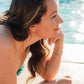 Woman sitting by a pool with water in the background wearing pink pearl earrings and matching necklace. 
