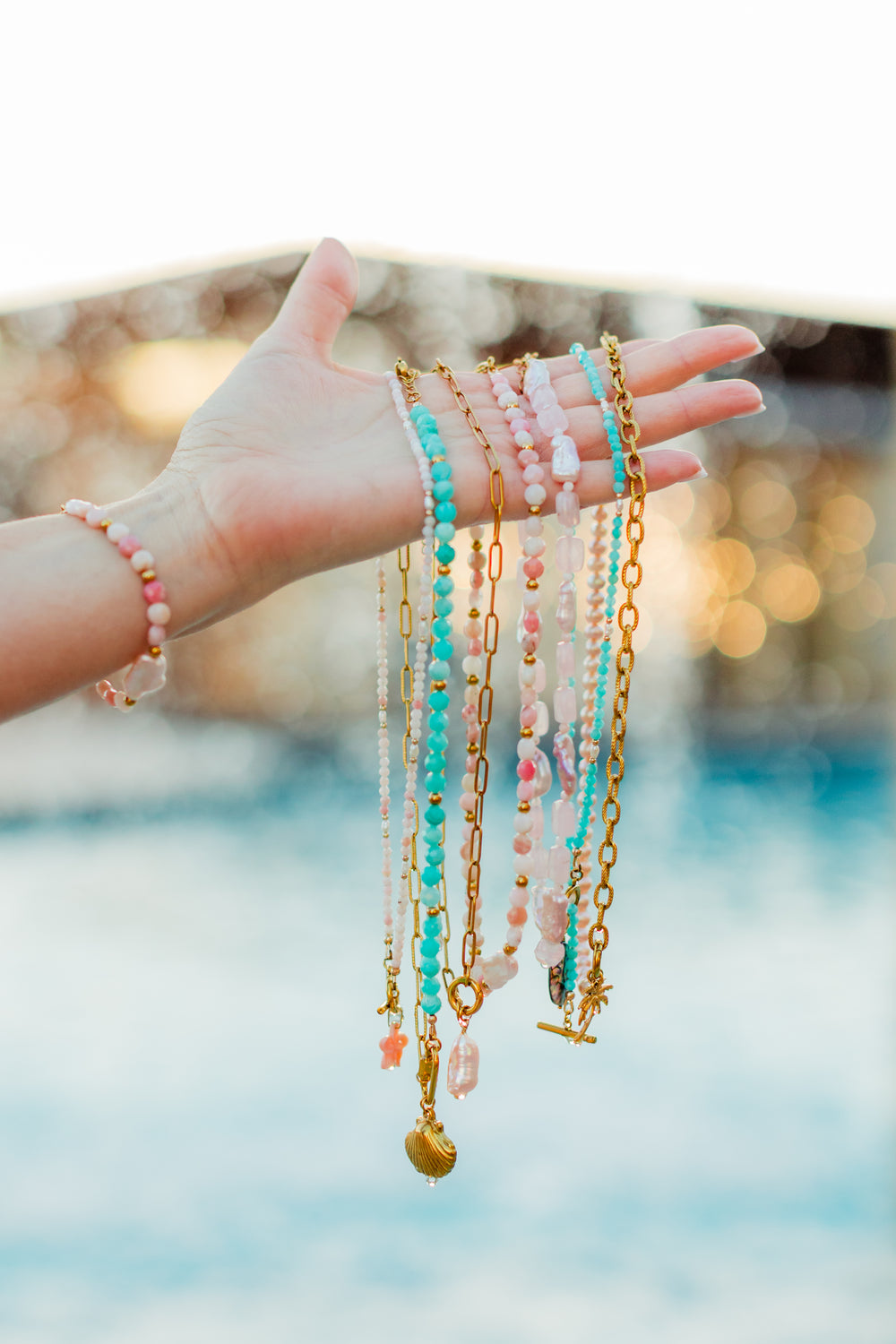 Hand wearing multiple necklaces with a blurred background