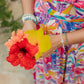 Person wearing a colorful dress holding two flowers, with a blurred natural background