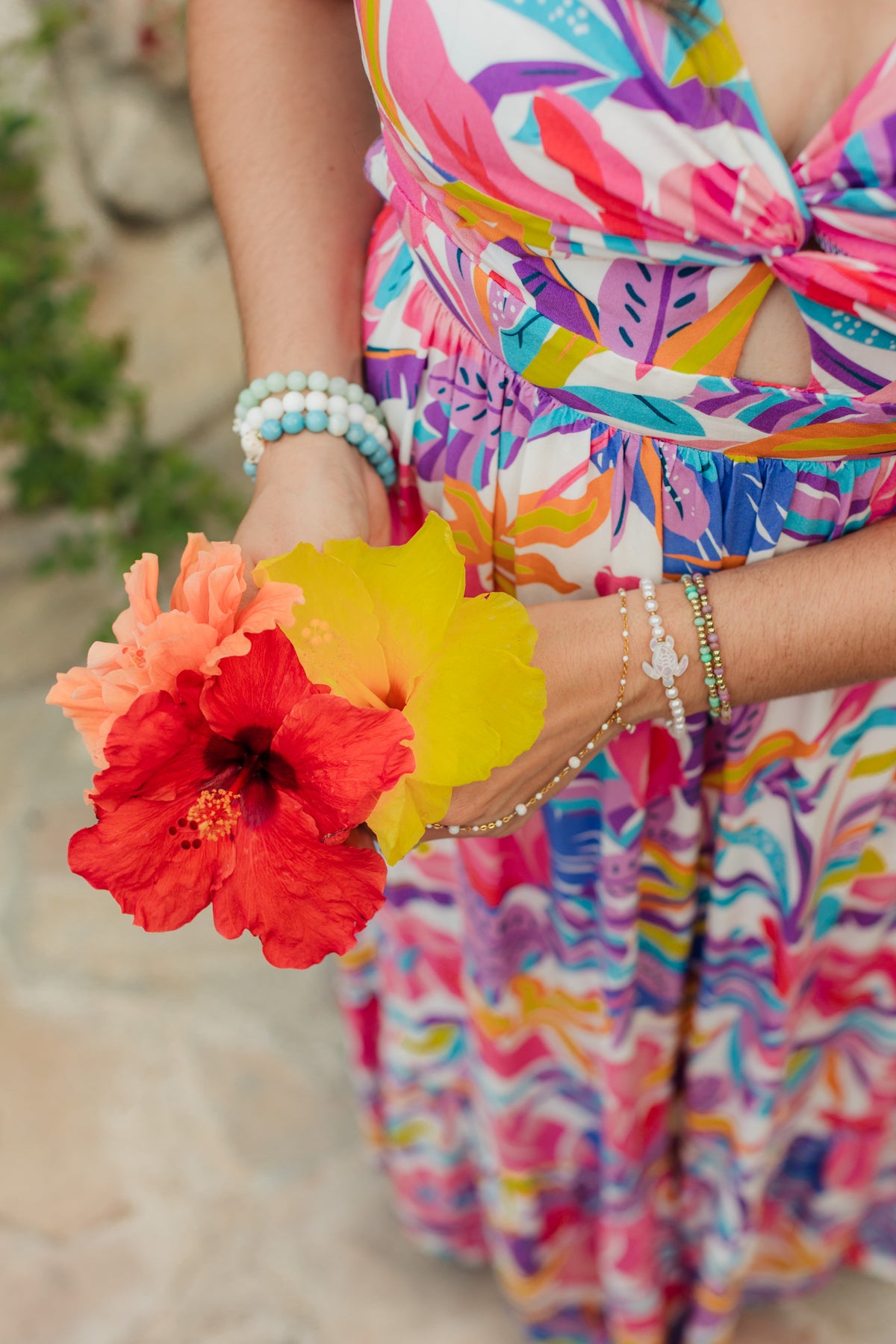 Person wearing a colorful dress holding two flowers, with a blurred natural background