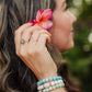 Woman with a pink flower in her hair and a stack of shell bracelets on her wrist, outdoors.