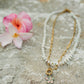 Necklace with a floral pendant on a stone surface with flowers in the background