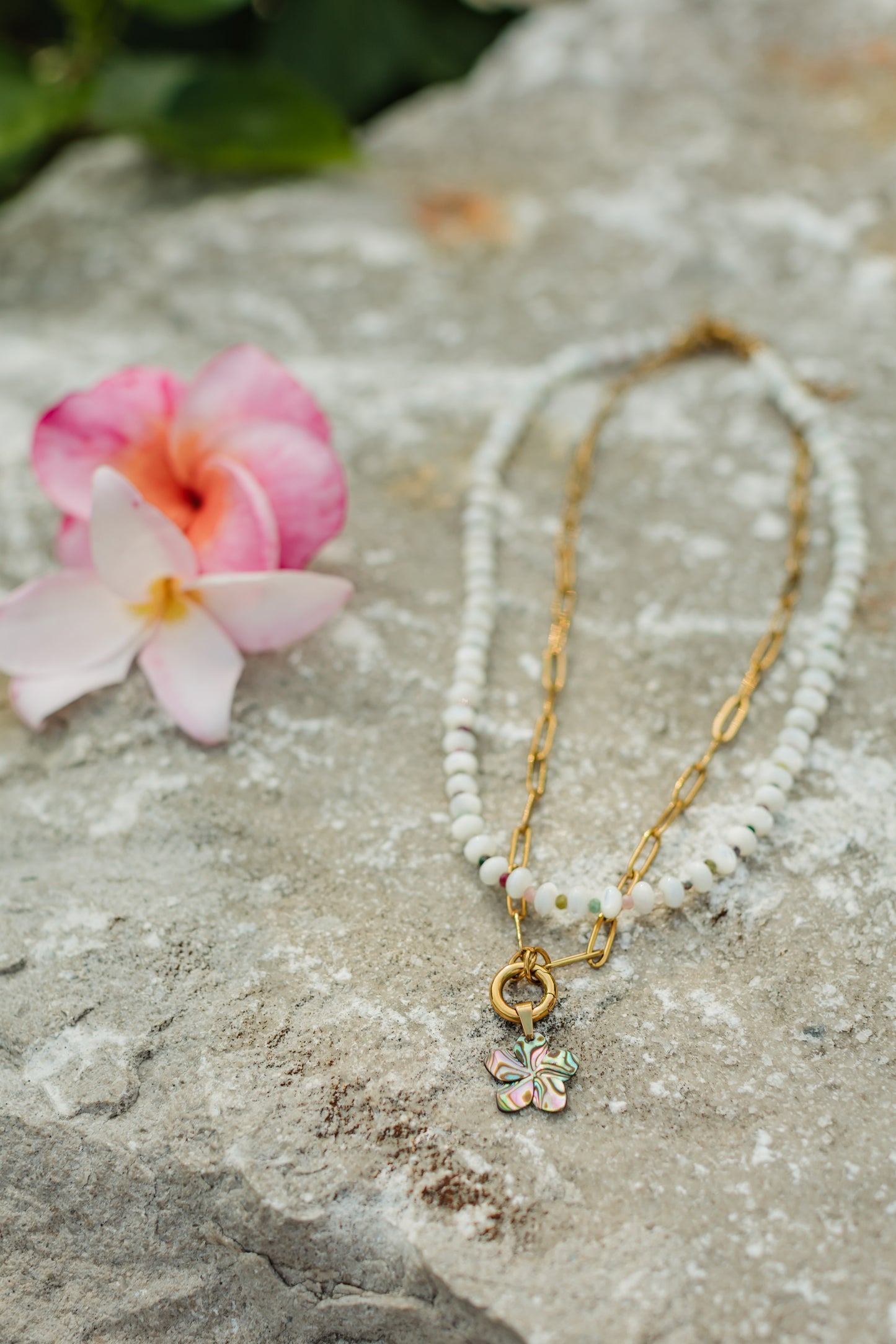 Necklace with a floral pendant on a stone surface with flowers in the background
