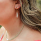 Close-up of a woman wearing gold earrings with white dangling stones.