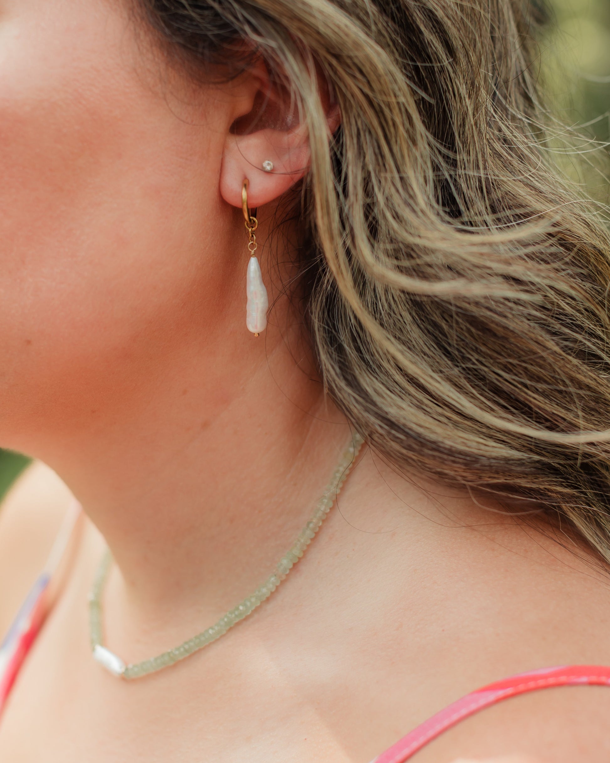 Close-up of a woman wearing gold earrings with white dangling stones.