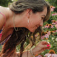 Woman smelling a flower in a field of pink flowers wearing ocean pearl drop earrings. 