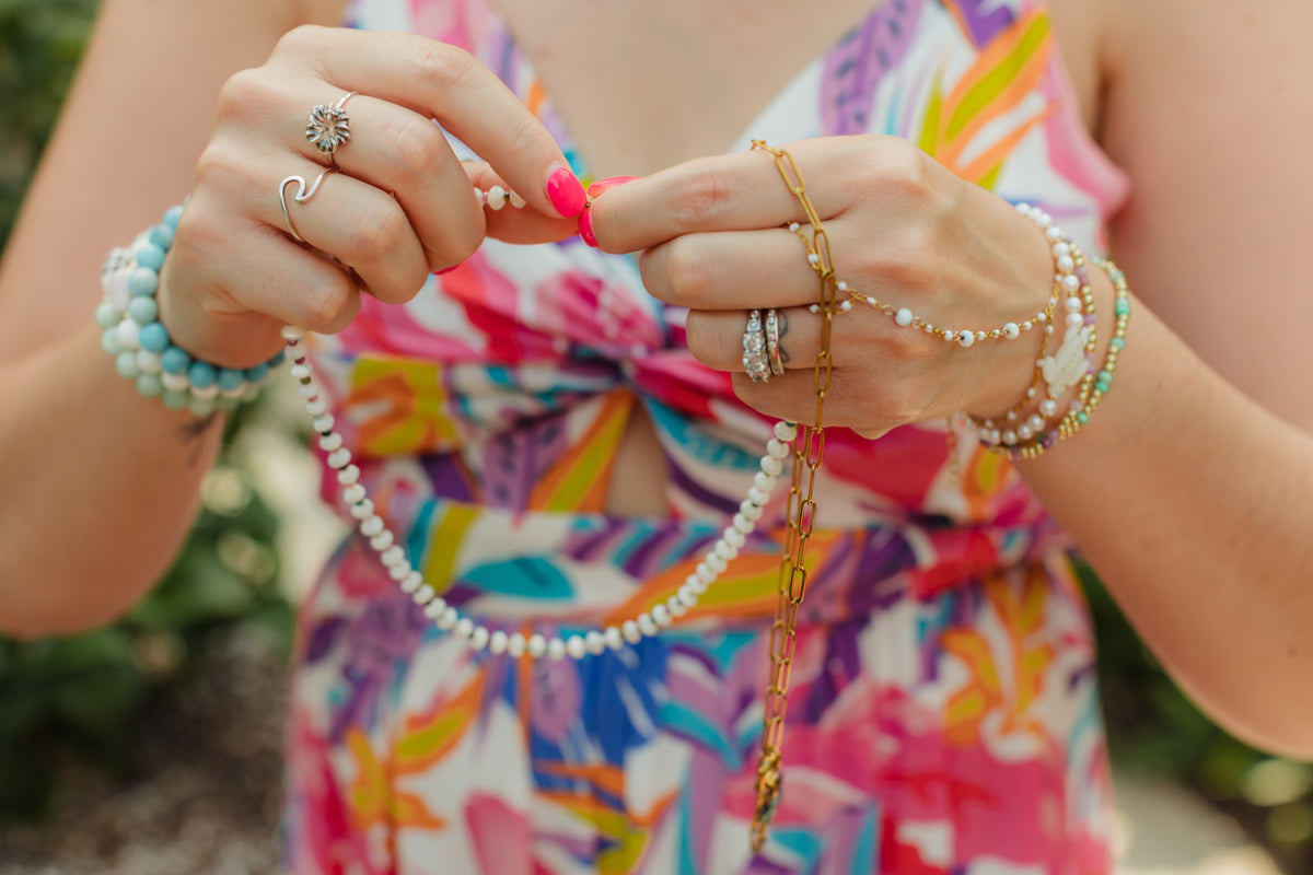 Person wearing multiple bracelets and rings with a colorful background