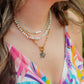 Woman wearing a colorful floral dress with layered necklaces and earrings outdoors.