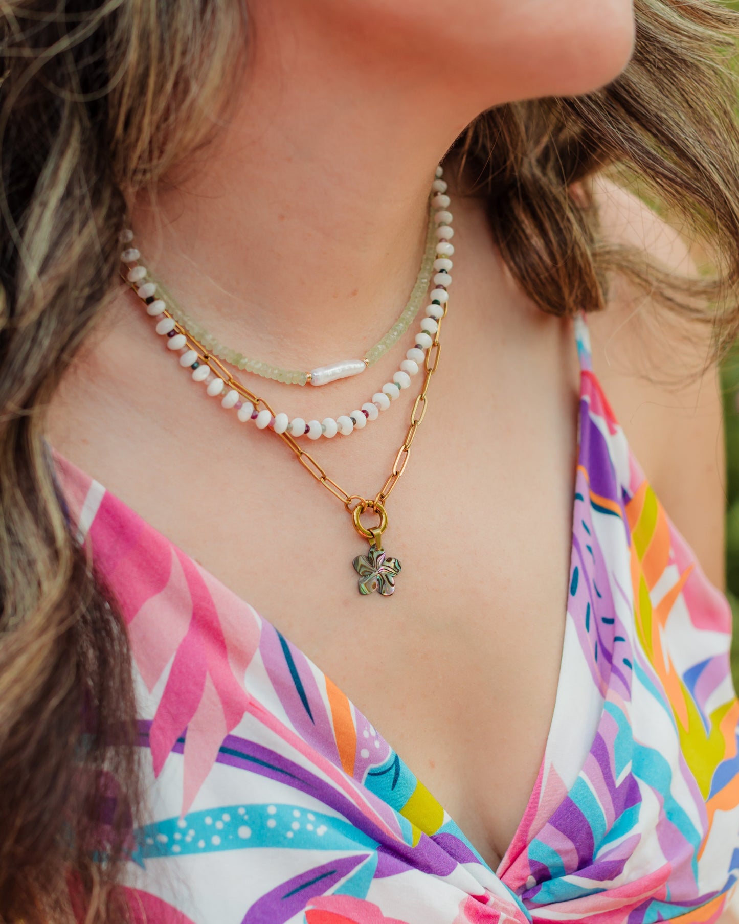 Woman wearing a colorful floral dress with layered necklaces and earrings outdoors.