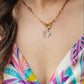 Woman wearing a colorful patterned top and a gold necklace with a maui bloom flower pendant.