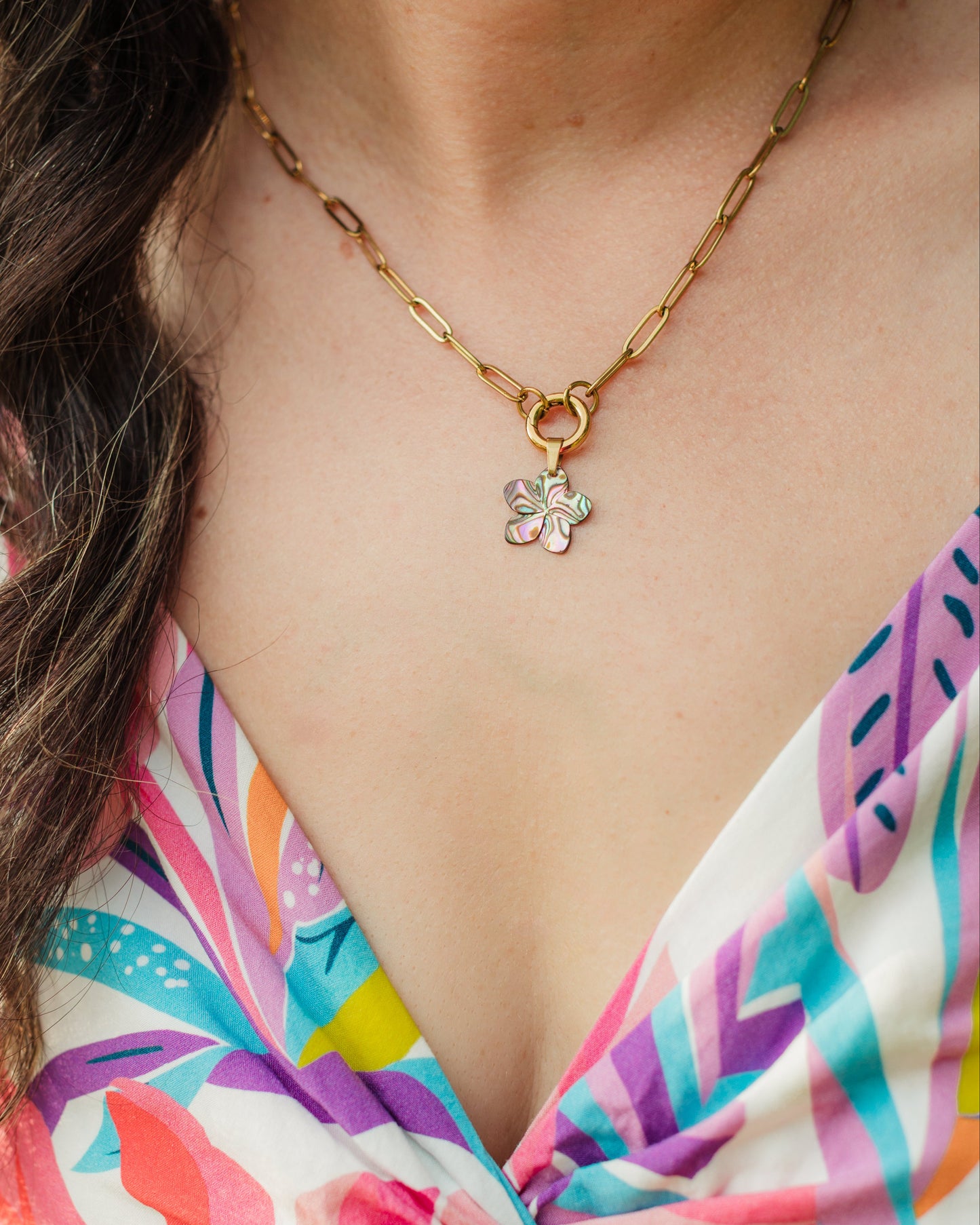 Woman wearing a colorful patterned top and a gold necklace with a maui bloom flower pendant.