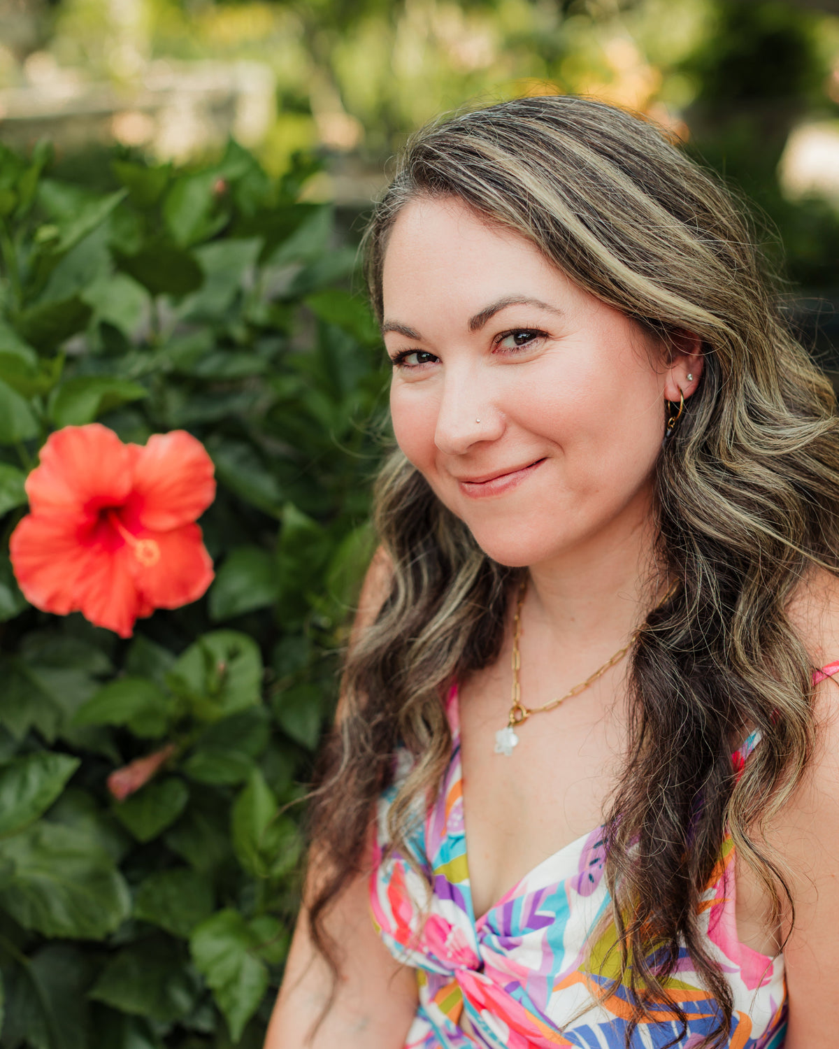 Woman in a colorful dress sitting outdoors with greenery and a red flower in the background