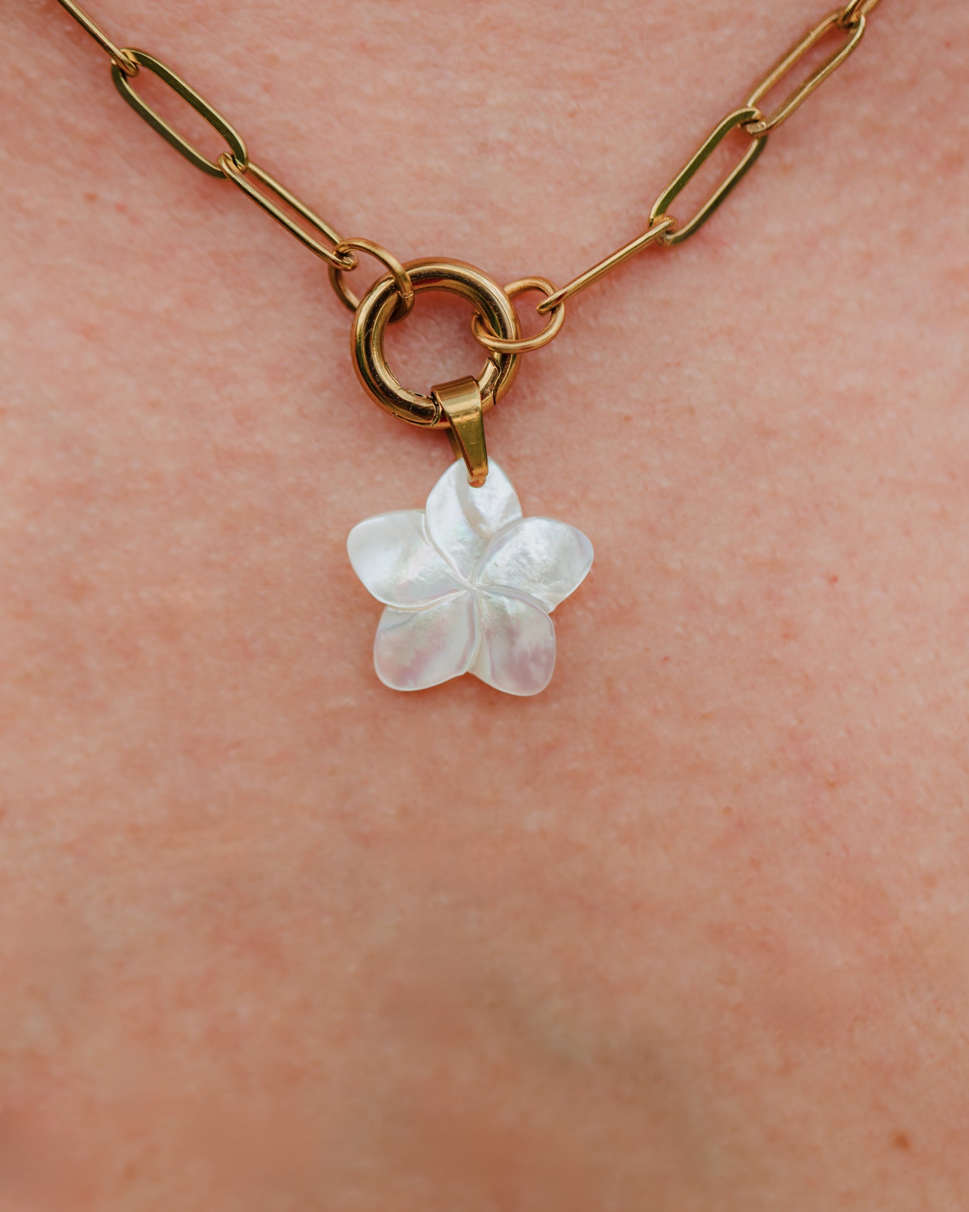 Gold chain necklace with a white flower pendant on skin