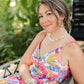 Woman in a colorful dress sitting outdoors with greenery in the background wearing the Leilani pearl necklace.