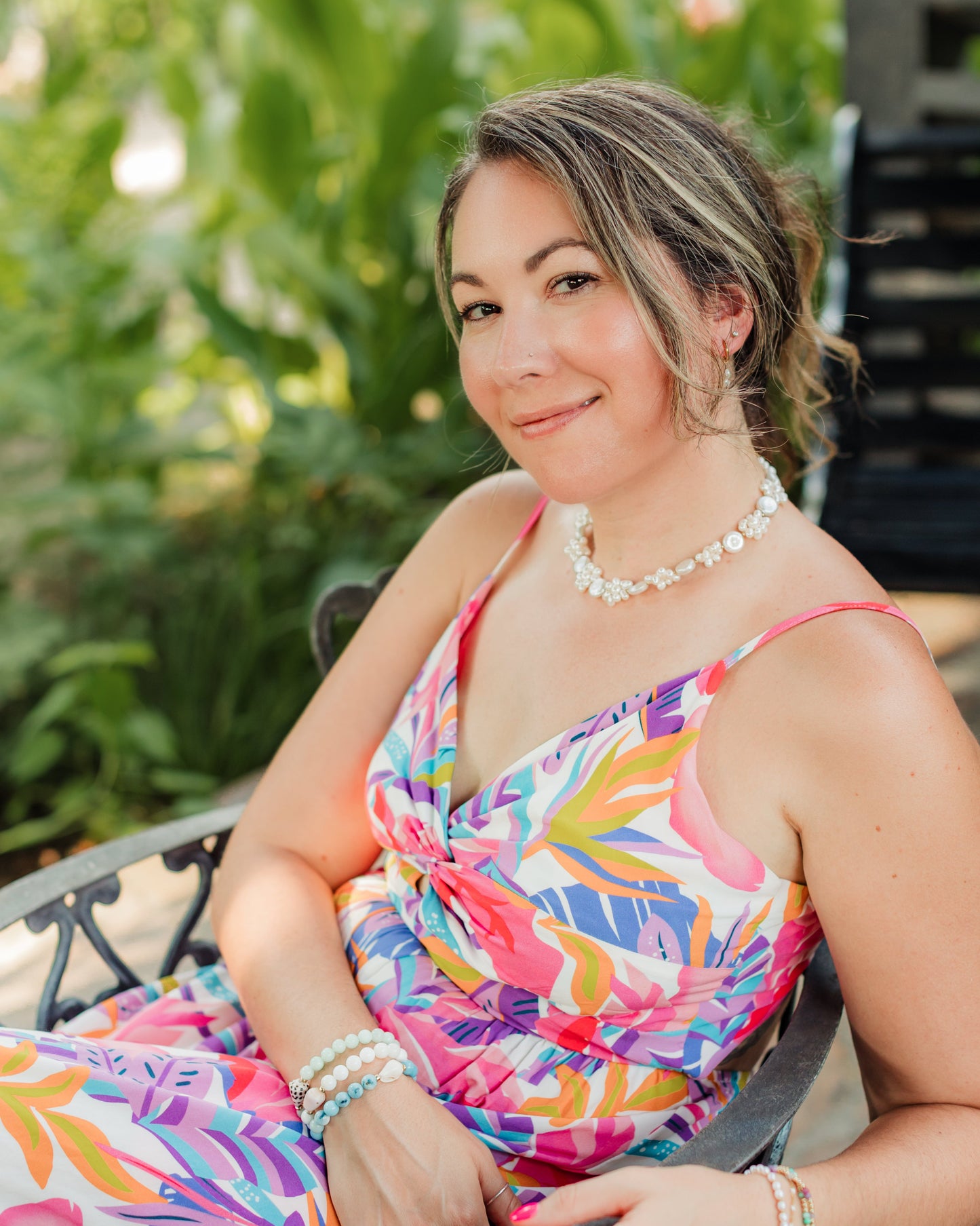 Woman in a colorful dress sitting outdoors with greenery in the background wearing the Leilani pearl necklace.