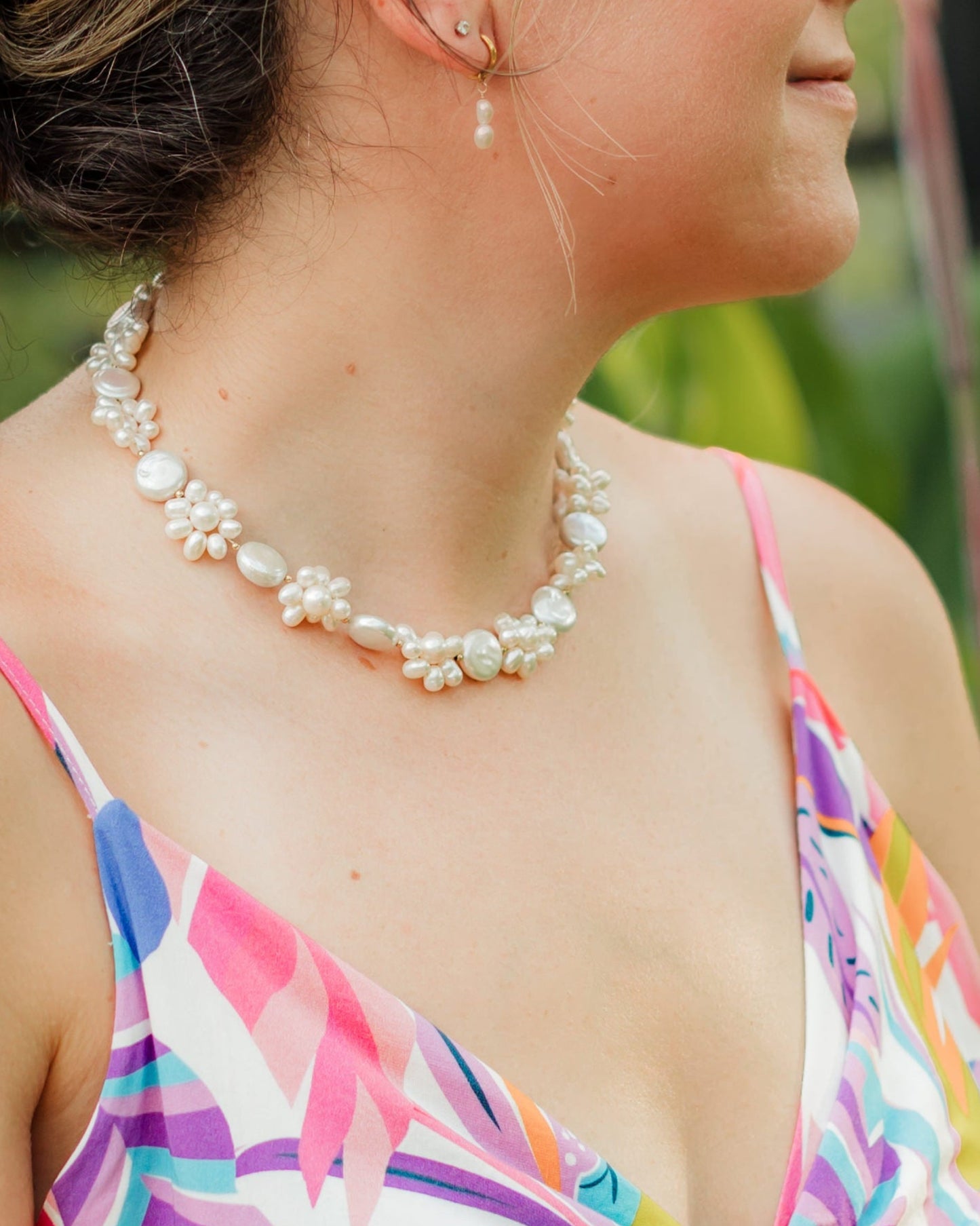 Woman in a colorful dress standing in a garden with orange flowers and greenery wearing Leilani flower pearl necklace.