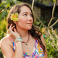 Woman in a colorful dress with a flower in her hair, standing in a garden.