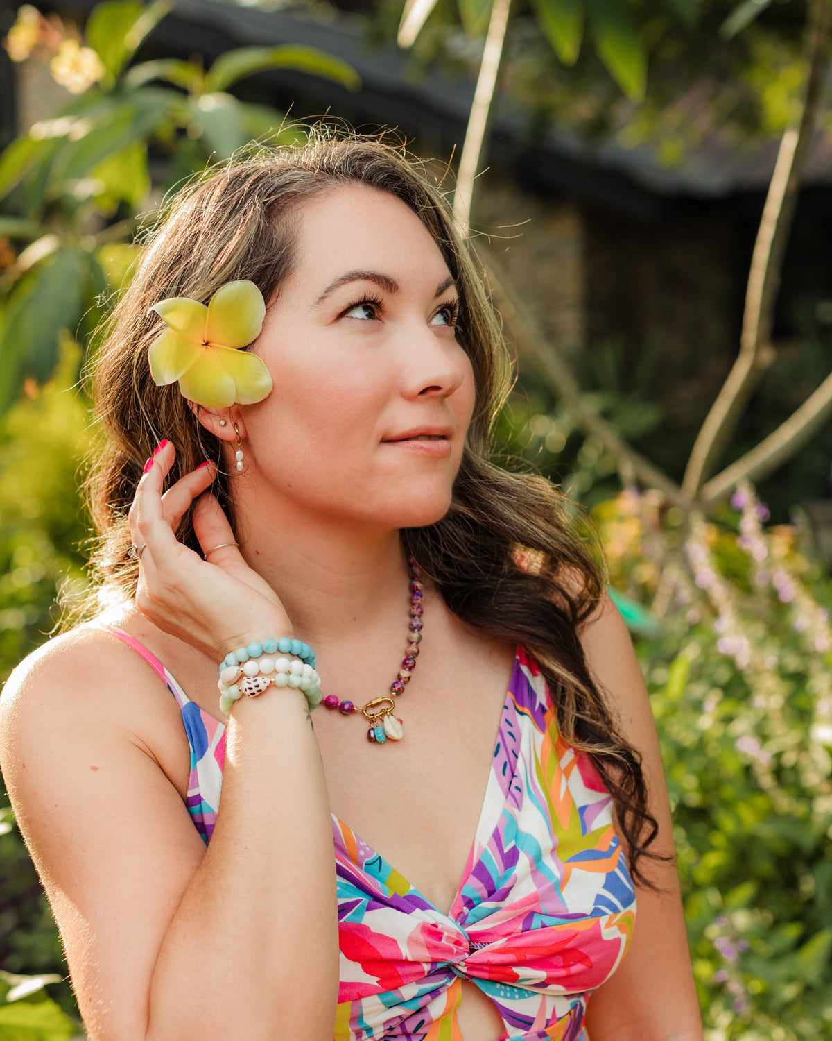 Woman in a colorful dress with a flower in her hair, standing in a garden.