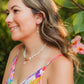 Woman in a colorful dress standing outdoors with greenery and flowers in the background wearing sunrise shell coral shell necklace and earrings.