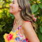 Woman in a colorful dress holding a yellow flower, surrounded by greenery