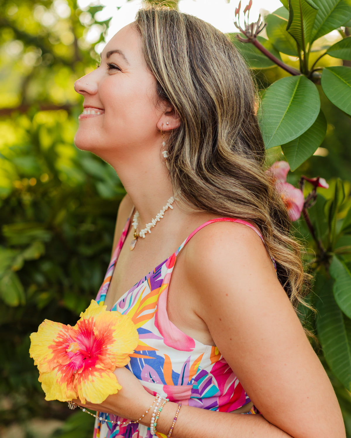 Woman in a colorful dress holding a yellow flower, surrounded by greenery