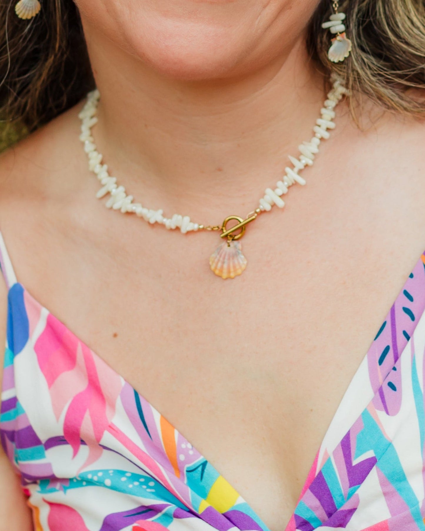Woman wearing a colorful dress with a blurred green background wearing Hawaiian sunrise shell necklace 