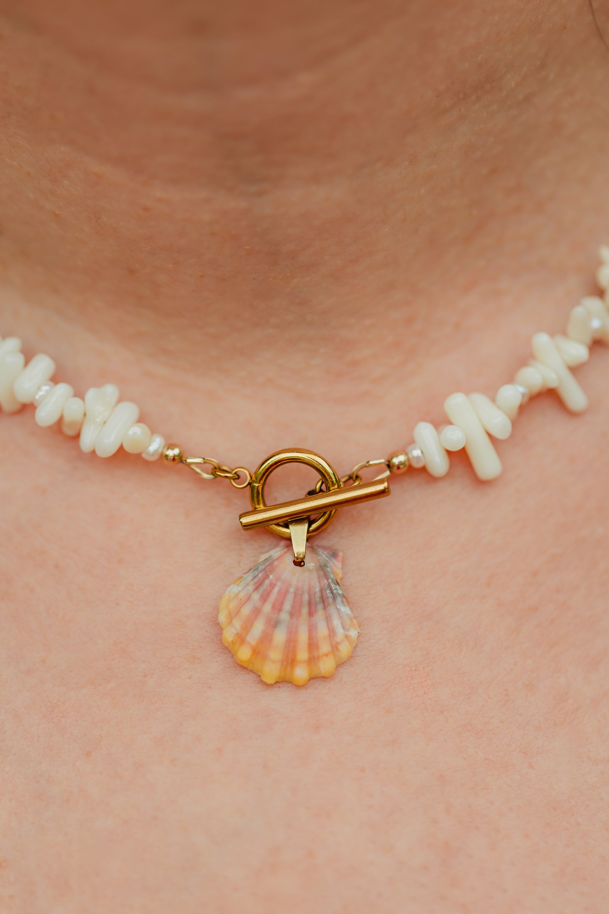 Hand-strung necklace featuring genuine coral chips, freshwater pearl accents, an authentic Hawaiian sunrise shell pendant, and an 18K Gold PVD toggle clasp inspired by the colors of Hawaiian sunrises.