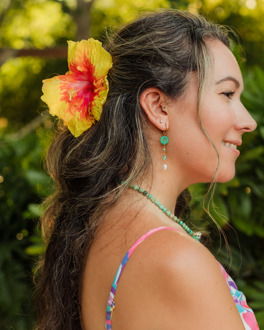 Woman wearing the Island Treasure Earrings with a colorful tropical flower in her hair and greenery behind her
