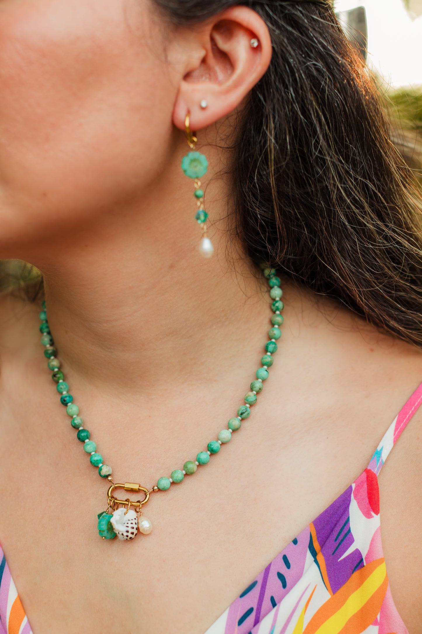 Hand-strung Peruvian turquoise gemstone necklace featuring an 18K Gold PVD oval carabiner clasp with removable charms including a turquoise Swarovski crystal, Czech glass hibiscus, Hawaiian spotted drupe shell, and freshwater pearl.