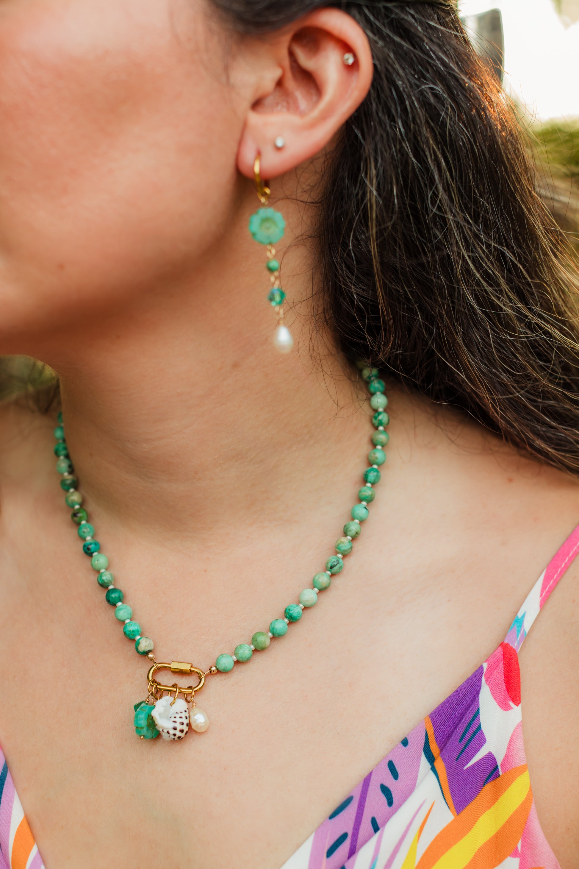 Hand-strung Peruvian turquoise gemstone necklace featuring an 18K Gold PVD oval carabiner clasp with removable charms including a turquoise Swarovski crystal, Czech glass hibiscus, Hawaiian spotted drupe shell, and freshwater pearl.