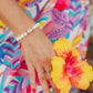 Person wearing a colorful dress holding a yellow flower wearing Lavender Bloom Bracelet with polished white shell beads, 14K gold-filled accents, and a rare natural lavender cone shell