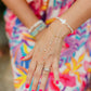 Close-up of a person's hand wearing multiple bracelets with a colorful dress in the background honu bracelet and hand chain