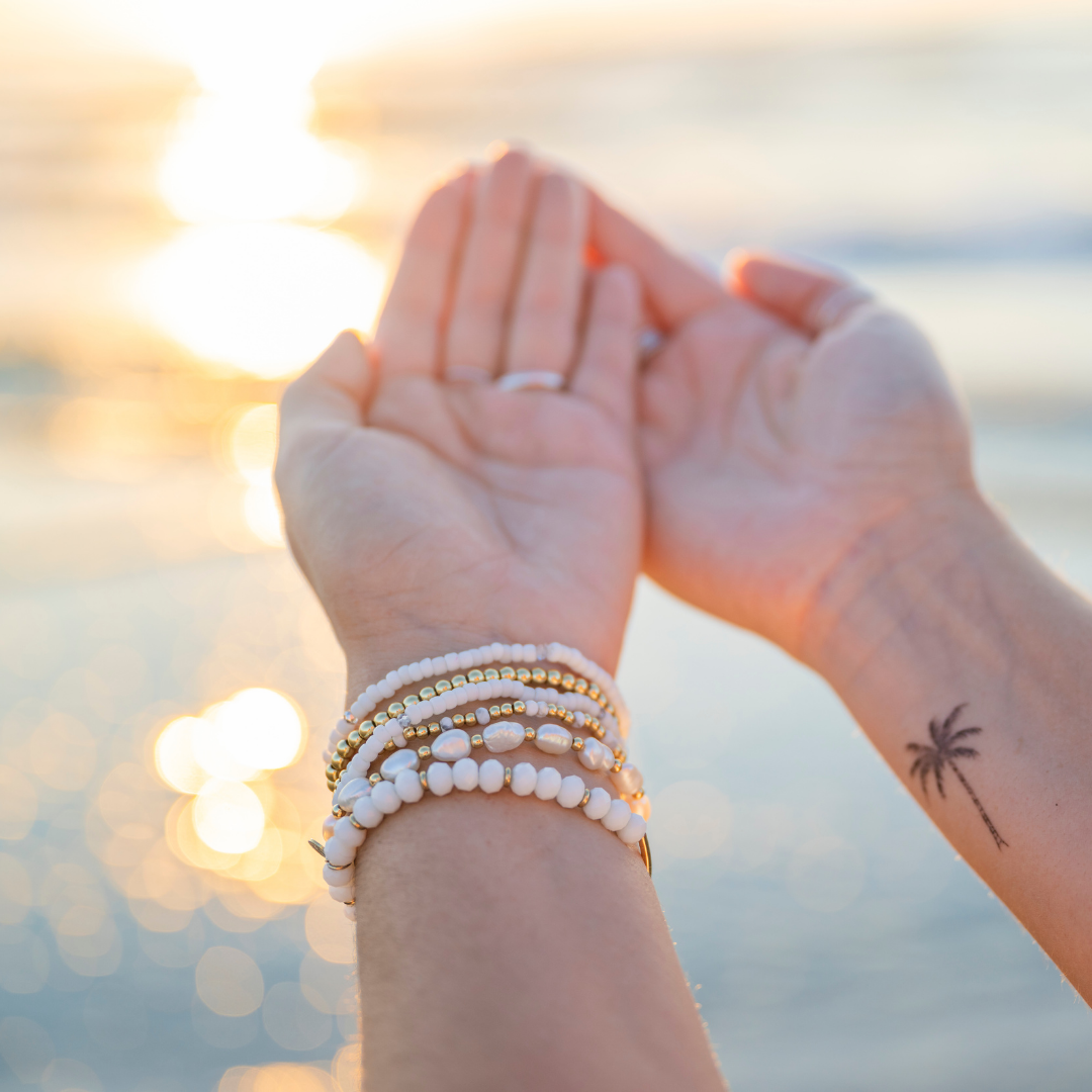 Two hands holding each other with sunset in the background  - Charlotte's Cove Jewelry Stacking bracelets