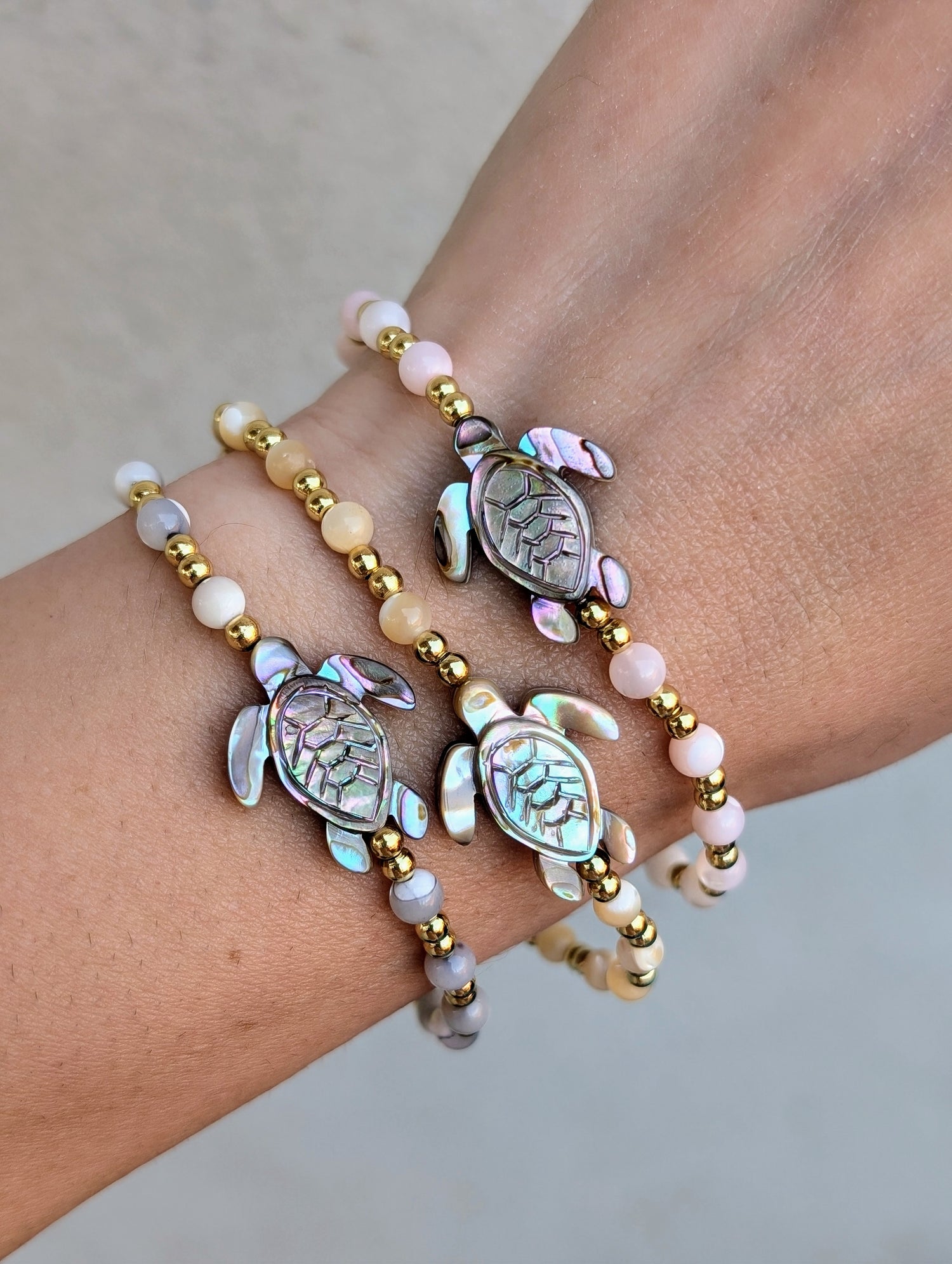 Close-up of an Abalone Sea Turtle Bracelet featuring a carved abalone shell turtle, mother of pearl accents, and 18K gold-filled beads, strung on a stretch cord.