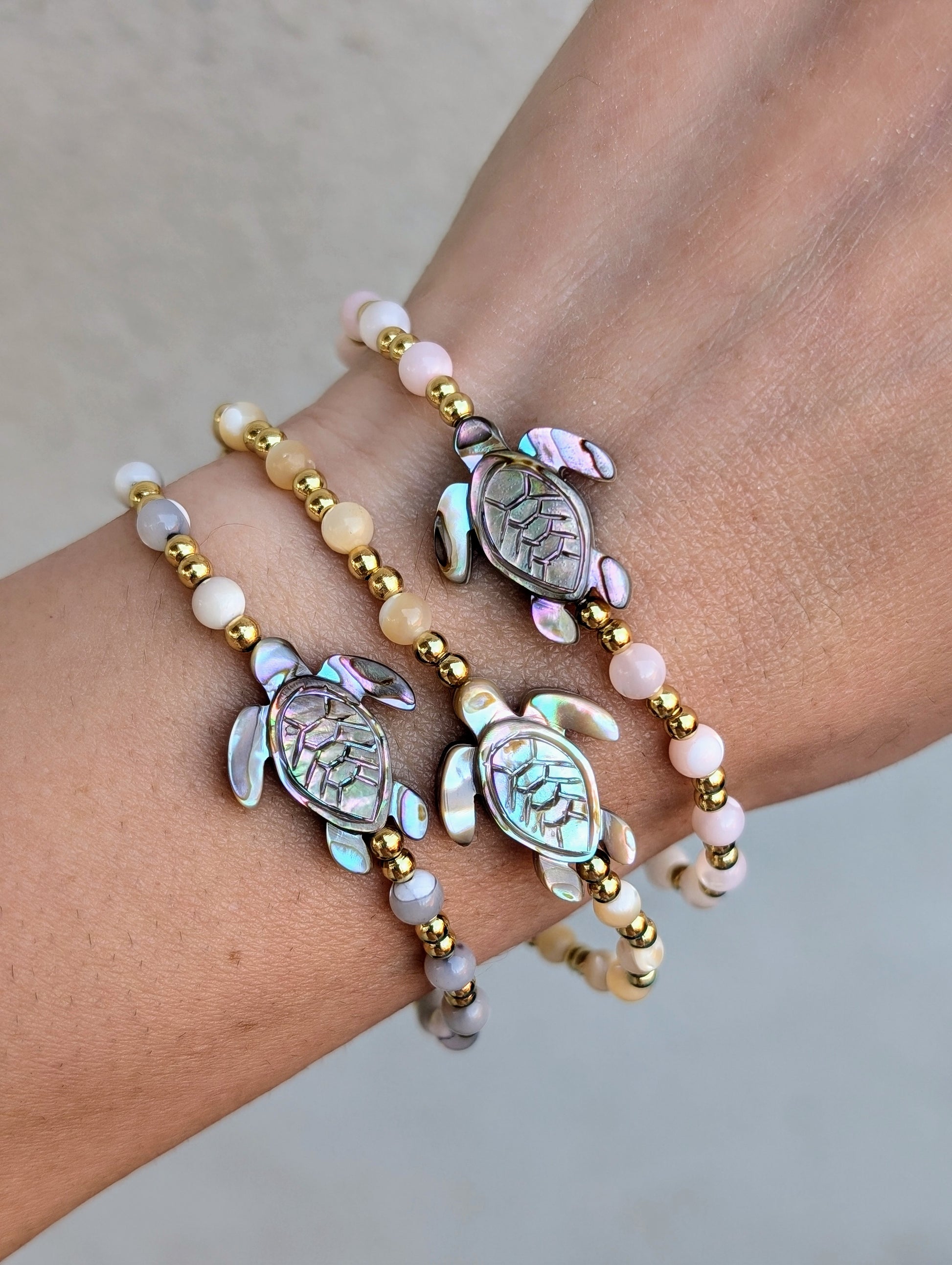 Close-up of an Abalone Sea Turtle Bracelet featuring a carved abalone shell turtle, mother of pearl accents, and 18K gold-filled beads, strung on a stretch cord.