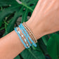 Wrist with blue beaded bracelets against a green leafy background