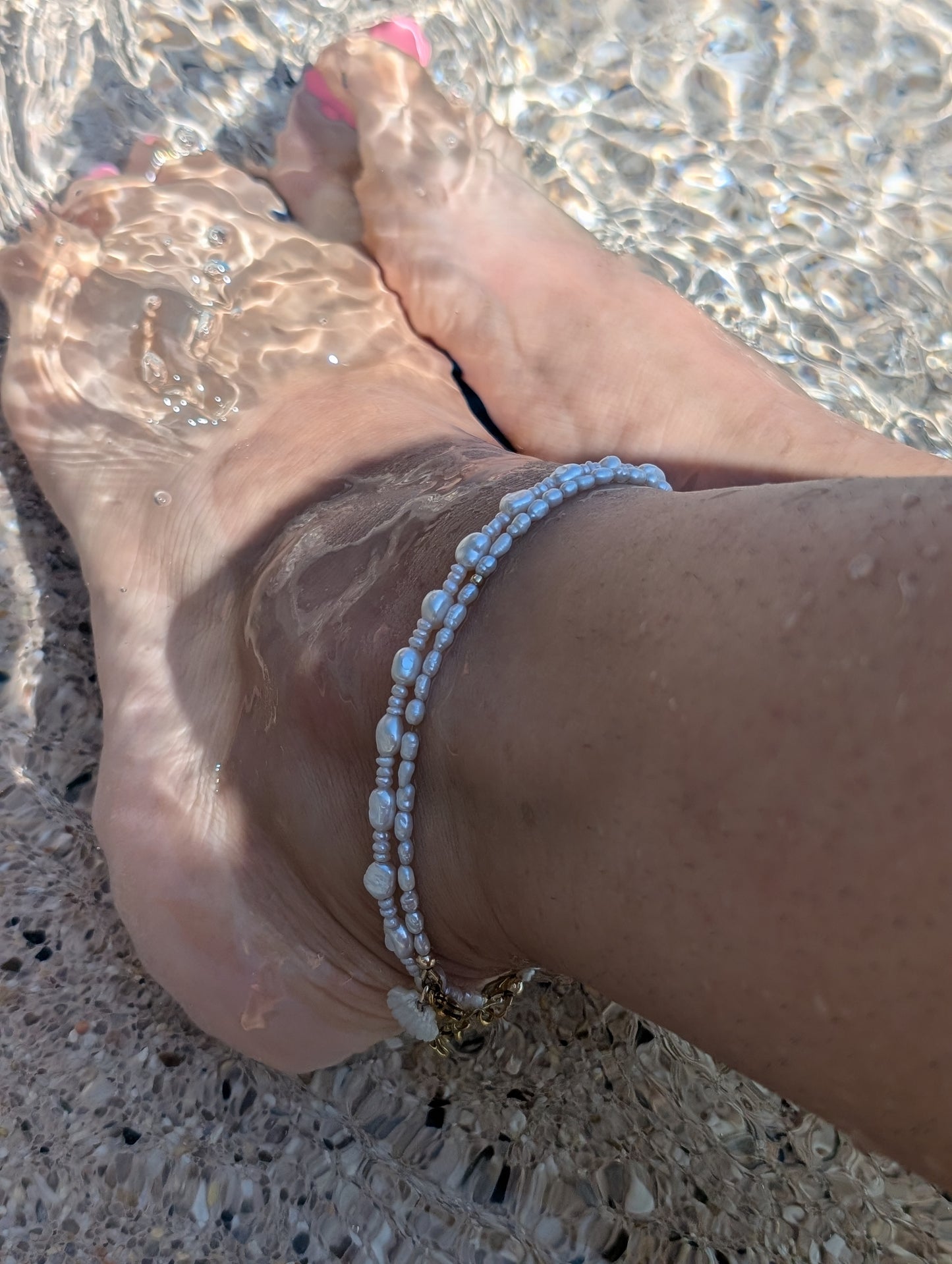 Layered pearl anklet styled with gold jewelry for a coastal summer look