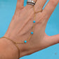 A gold chain hand and wrist bracelet with small turquoise blue beads, shown worn on a person's hand against a bright blue background.
