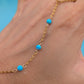 A close-up of a hand wearing a delicate gold chain anklet with three small bright turquoise blue beads spaced along the chain.