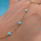 A delicate gold chain bracelet worn on a hand, featuring three small round light blue opal beads spaced along the chain.