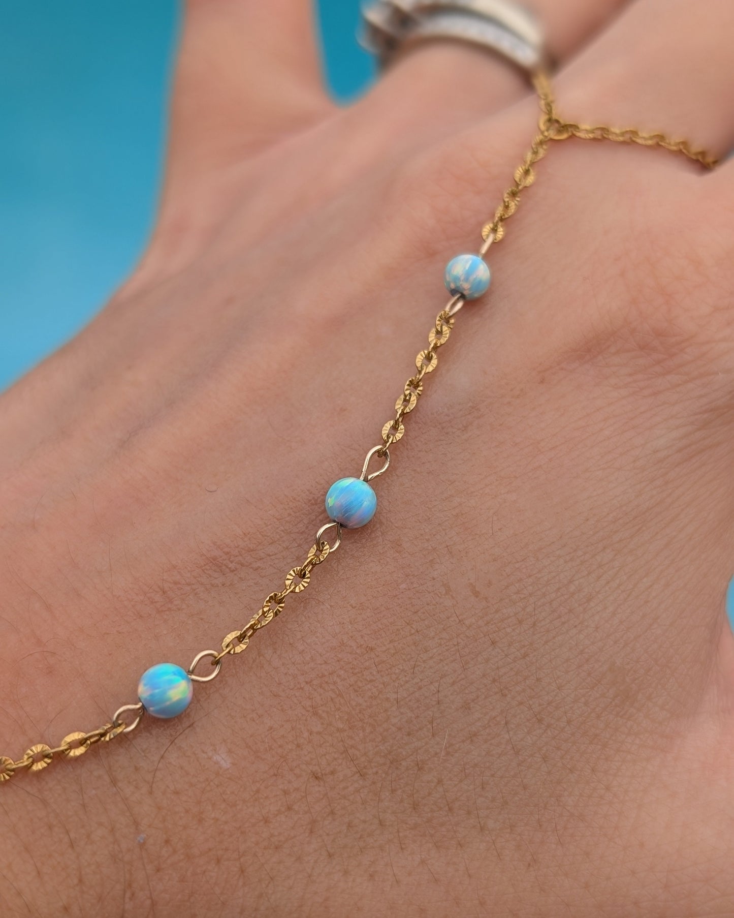 A delicate gold chain bracelet worn on a hand, featuring three small round light blue opal beads spaced along the chain.