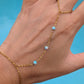 A gold chain hand bracelet with four small light blue beads, shown worn on a hand against a bright blue background.