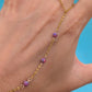 A gold chain anklet with three small purple marbled beads worn on a person's ankle, shown against a bright blue background.