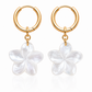 Gold hoop earrings with white flower charms on a white background