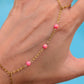 A gold chain hand and wrist bracelet with small pink beads, shown worn on a person's hand against a bright blue background.