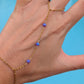 A gold chain hand bracelet with four small blue beads worn on a person's hand, shown against a bright blue background.